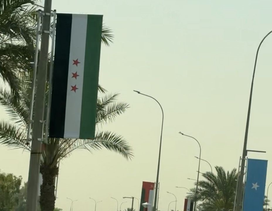 رغم الرفض الشعبي لحضور الشرع إلى القمة العربية… العلم السوري الجديد يٌرفع في شوارع بغداد